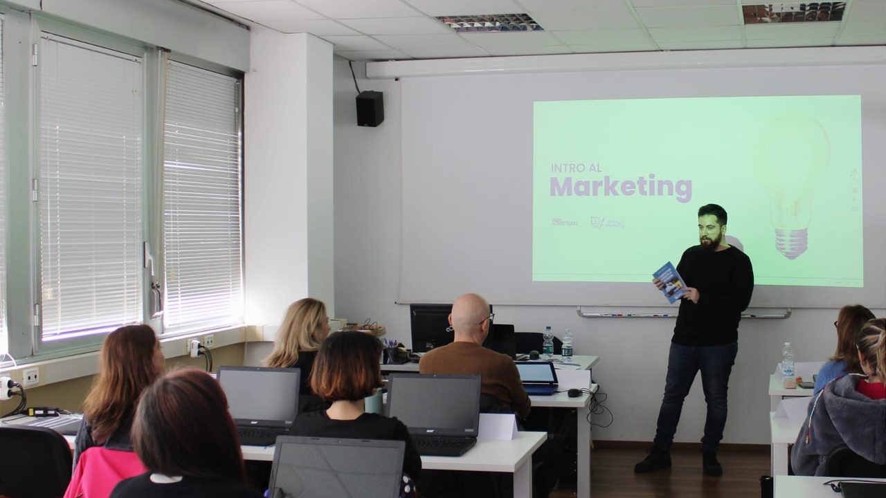 Stefano Antonucci in aula con in mano un libro, davanti alla slide «Intro al Marketing»
