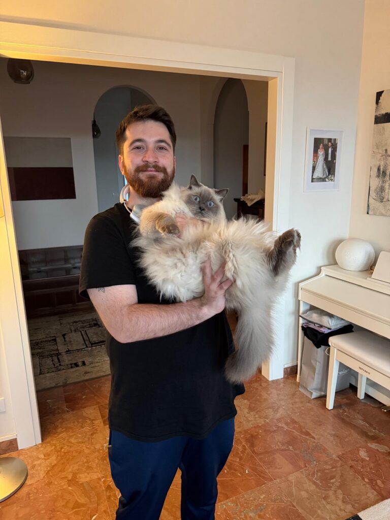 WhatsApp Image 2026-05-14 at 16.51.04 A man with a beard holds a large fluffy cat indoors, smiling at the camera.